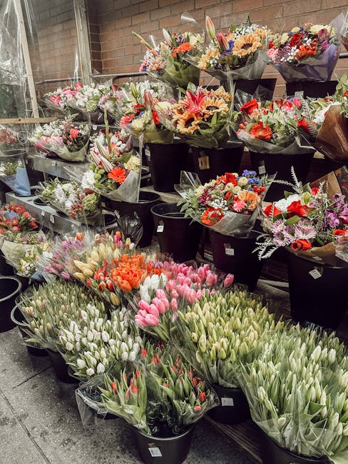 An indoor display of numerous flower bouquets and arrangements showcases a variety of fresh flowers including pink and white tulips, orange lilies, and mixed seasonal blooms. The bouquets are wrapped